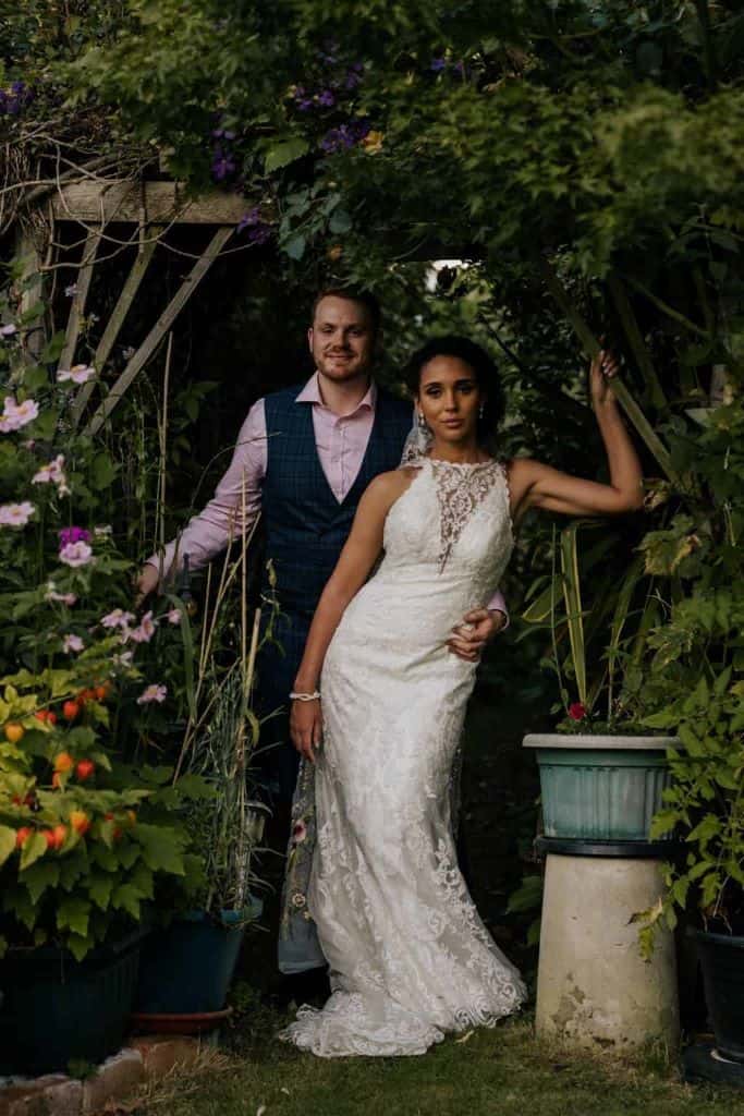 Mixed-race bride rocking a curly bridal bun and veil standing with her husband in front of a garden arch.