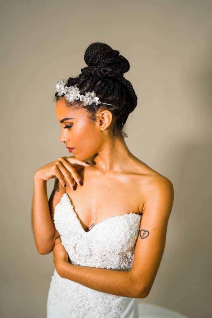 A model bride styled by Brides by Aina.M with natural makeup and an updo twist hairstyle with a floral headband gently touching her chin.
