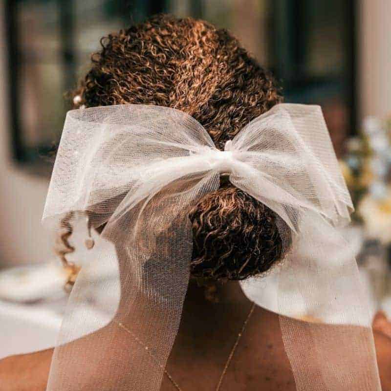 Mixed race bride wearing her curly hair in an elegant twisted updo accessorised with a classic organza bow.