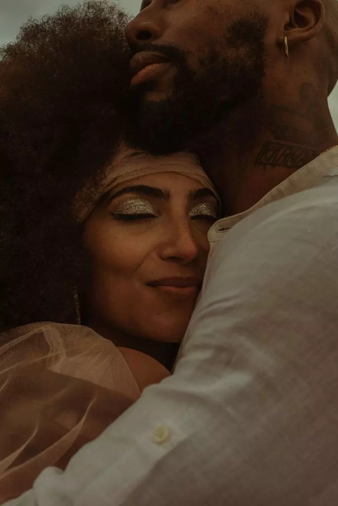Bride wearing bridal afro and headband, paired with soft glam bridal makeup, embracing her fiancé.
