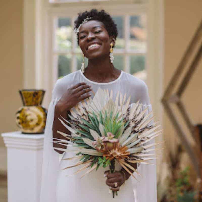 Black natural hair and makeup bride holding an exotic bouquet of flowers smiling.